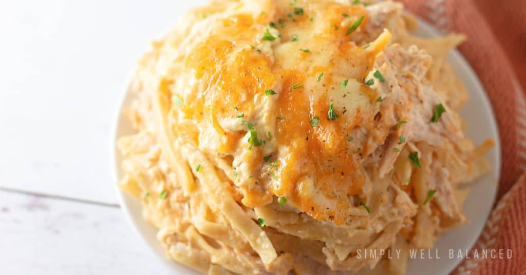A serving of cheesy chicken tetrazzini casserole on a white plate next to an orange cloth napkin. 