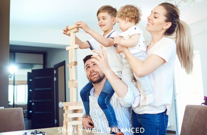 A mother and father playing with minimalist wooden block toys with two young boys, demonstrating it's possible to live minimalism with kids.