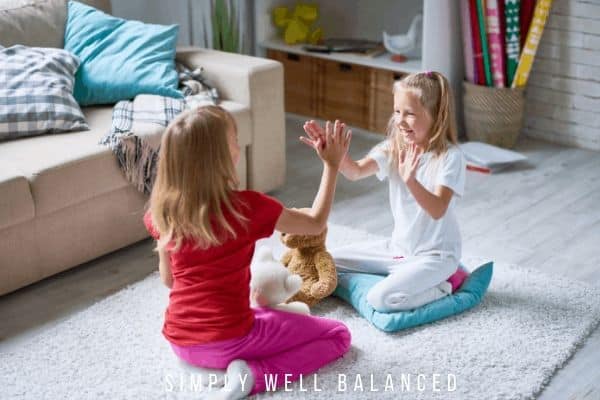 Two girls playing hand clapping games on the living room floor