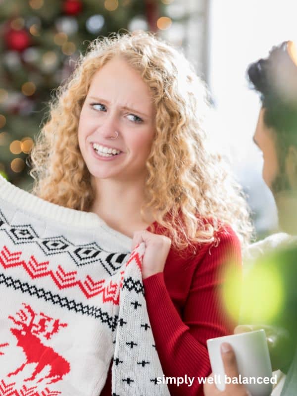 Woman opening an ugly Christmas sweater gift, with a confused look on her face. 