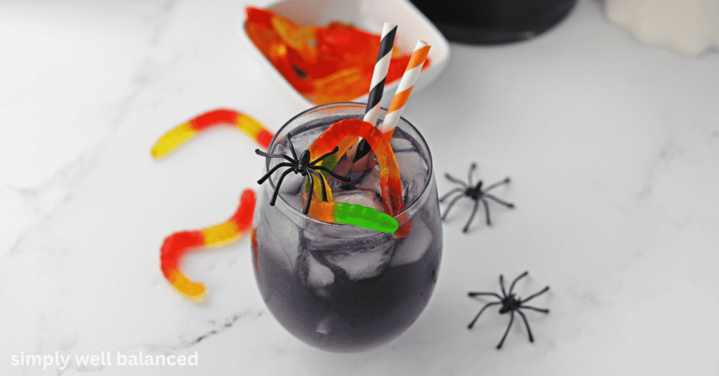 Non-alcoholic purple Halloween Punch with striped paper straws and plastic spiders on the counter. 